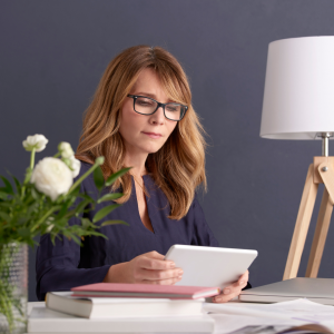 Woman with glasses reading tablet at desk