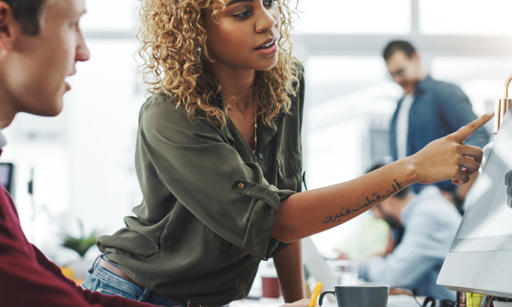 Woman pointing to a screen at colleague's desk