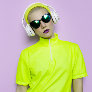 Woman in sunglasses, headphones, and neon yellow outfit against lilac background