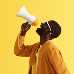 A man shouting into a megaphone in front of a yellow background