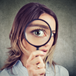 Woman holding magnifying glass to eye examining