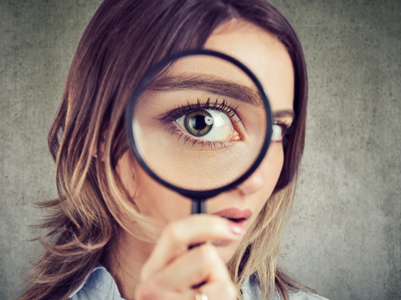 Woman holding magnifying glass to eye examining